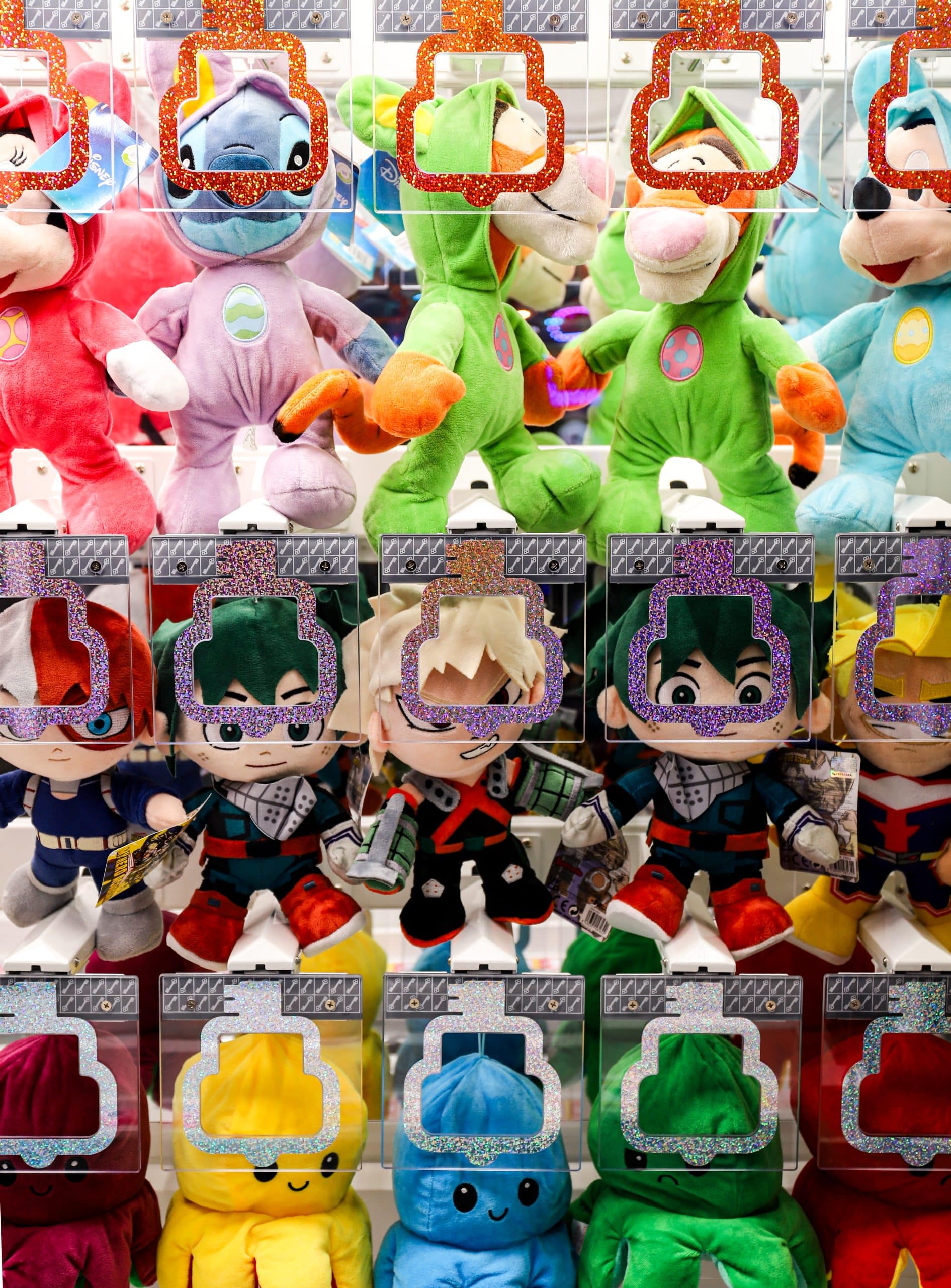 Peluches colorées dans une machine à pinces d'arcade, incluant des personnages Disney, My Hero Academia et des pieuvres en peluche multicolores.